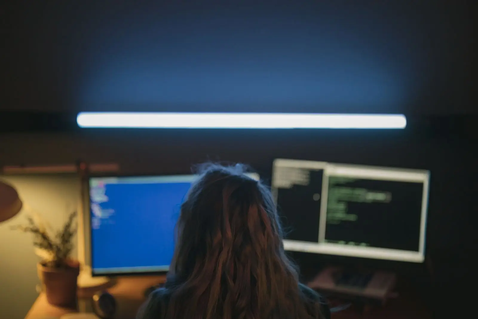 A developer working at two monitors in a dim room